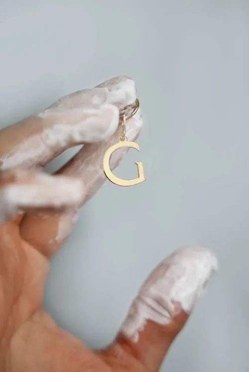 Hand mit Schaum hält einen goldenen Buchstabenanhänger «G» von Giada Ilardo.