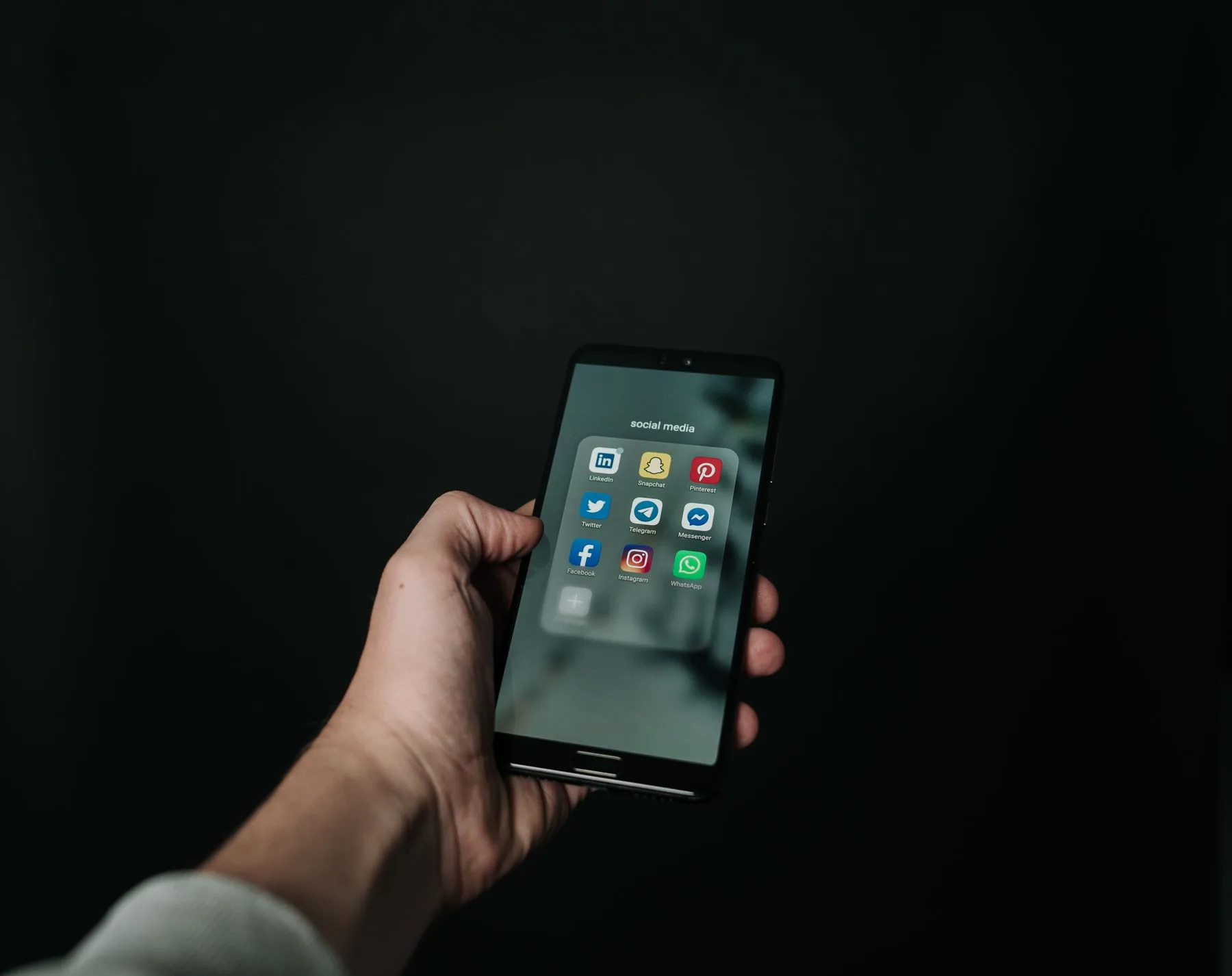 Hand hält ein Smartphone mit geöffnetem Ordner voller Messenger- und Social-Media-Apps.